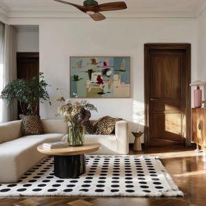 May include: A living room featuring a cream-colored sectional sofa with leopard print pillows, a round wooden coffee table with a black base, and a white area rug with black polka dots. A framed painting of flying birds hangs on the white wall.