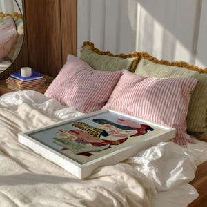 May include: A framed artwork featuring a colorful illustration of cowboy boots. The boots showcase various patterns and textures, including leopard print and floral designs. The artwork is displayed on a bed with striped pillows.
