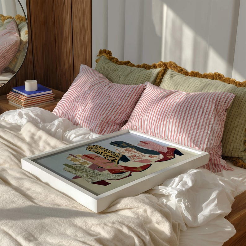 May include: A framed artwork featuring a colorful illustration of cowboy boots. The boots showcase various patterns and textures, including leopard print and floral designs. The artwork is displayed on a bed with striped pillows.