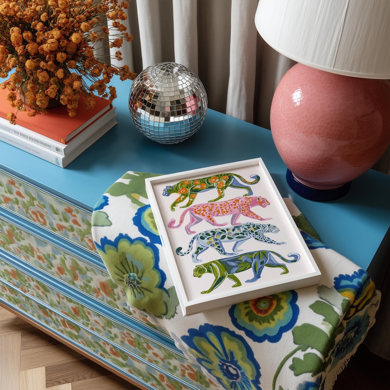 Four prowling leopards in vivid green, pink, sky-blue and indigo coats, each with whimsical floral patterns, stride across a cream backdrop. The bold dopamine palette enlivens living rooms, nurseries or eclectic gallery walls.