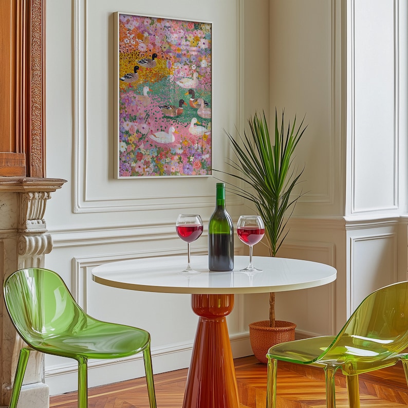 May include: A dining scene with a round white table on an orange base, two clear green chairs, and a framed painting of ducks in a floral setting. A green wine bottle and two glasses of red wine are on the table.