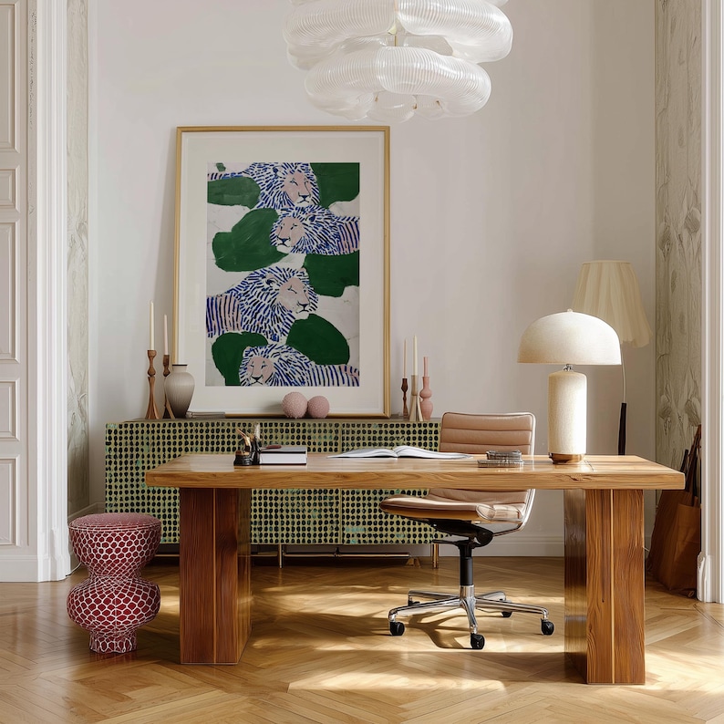 May include: An interior design scene featuring a wooden desk, a patterned cabinet, and a framed artwork with lion illustrations. A desk lamp, a chair, and a decorative stool are also present. The room is illuminated by natural light and a modern chandelier.