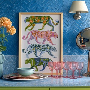 Four prowling leopards in vivid green, pink, sky-blue and indigo coats, each with whimsical floral patterns, stride across a cream backdrop. The bold dopamine palette enlivens living rooms, nurseries or eclectic gallery walls.