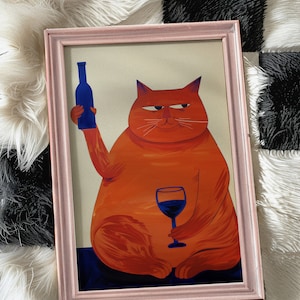 May include: A framed illustration of an orange cat holding a glass of red wine and a blue bottle of wine. The cat has a sly expression on its face.