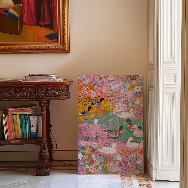 May include: A vibrant painting depicting ducks amidst a floral setting. The artwork showcases ducks with black and white patterns, set against a backdrop of pink, yellow, and green flowers. The painting is displayed in a room with a wooden table and a framed painting.