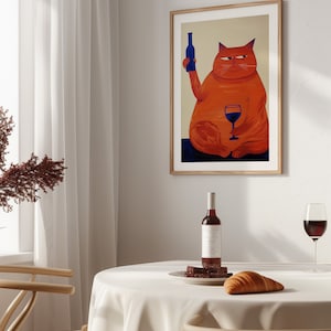 May include: A framed illustration of a red cat holding a bottle of wine in one paw and a glass of red wine in the other. The cat is sitting on a blue surface. The frame is made of wood and has a light brown finish.