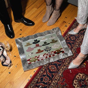 May include: A decorative mirrored tray featuring a collection of illustrated hats in various colors and patterns. The tray is surrounded by a mosaic border and rests on a wooden floor. The hats include designs such as a black fedora, a pink hat with a bow, and a cow-print hat.