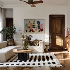 May include: A living room scene featuring a cream-colored sofa with leopard print pillows, a black and white polka dot rug, and a wooden coffee table. A framed painting of colorful cowboy boots hangs on the wall.