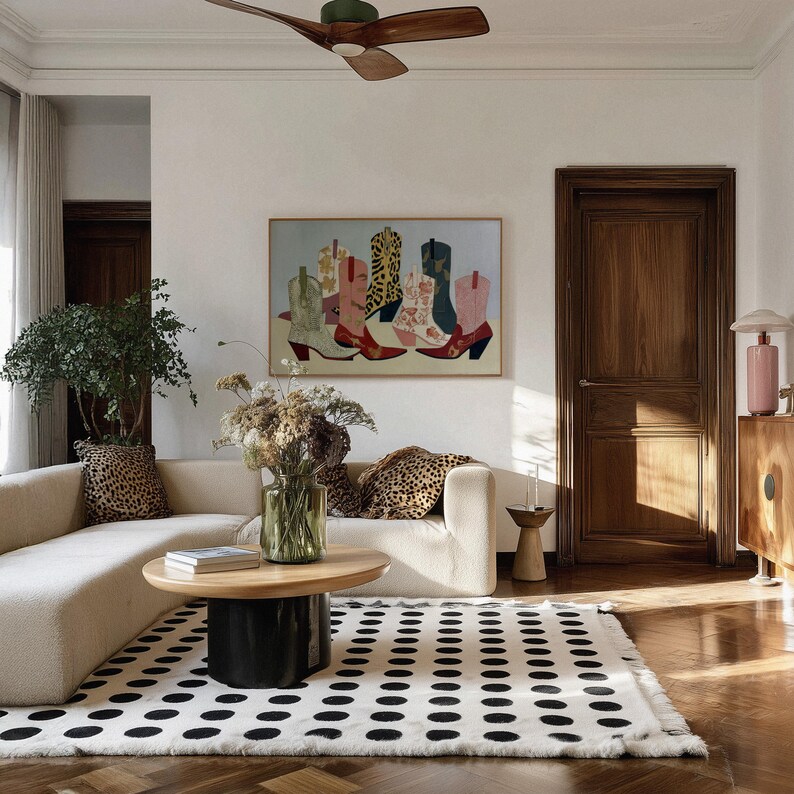 May include: A living room scene featuring a cream-colored sofa with leopard print pillows, a black and white polka dot rug, and a wooden coffee table. A framed painting of colorful cowboy boots hangs on the wall.