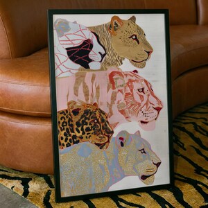 May include: A framed rectangular wall art print featuring four stacked big cat heads in profile. The top cat is tan, the second is pink with white stripes, the third is a yellow leopard with black spots, and the bottom cat is light blue.
