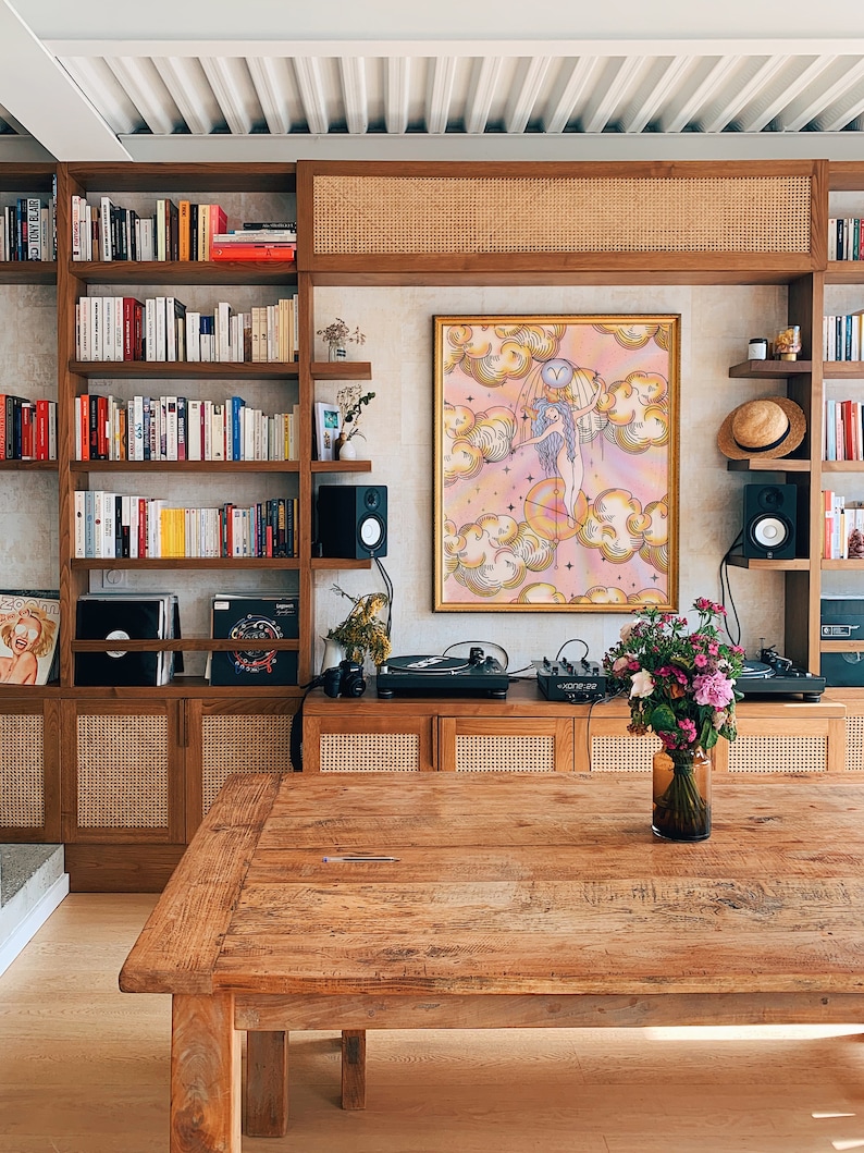 Puede incluir: Una mesa de madera con un acabado de madera clara. La mesa est&aacute; en una habitaci&oacute;n con una estanter&iacute;a, un tocadiscos y una impresi&oacute;n enmarcada de una mujer de pie en las nubes. La impresi&oacute;n tiene un esquema de color rosa, amarillo y azul.