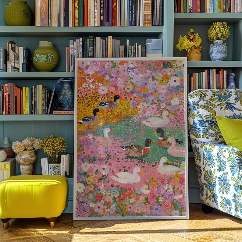 May include: A framed artwork depicting ducks amidst a colourful floral arrangement. The painting features a variety of flowers in pink, yellow, and white, with ducks dotted throughout. The artwork is displayed in a room with bookshelves and a patterned armchair.
