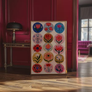 May include: A framed art print featuring a grid of colorful floral designs in circular patterns. The flowers are depicted in various styles and colors, including red, blue, yellow, and pink, set against a white background. The frame is gold.