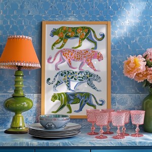 Four prowling leopards in vivid green, pink, sky-blue and indigo coats, each with whimsical floral patterns, stride across a cream backdrop. The bold dopamine palette enlivens living rooms, nurseries or eclectic gallery walls.