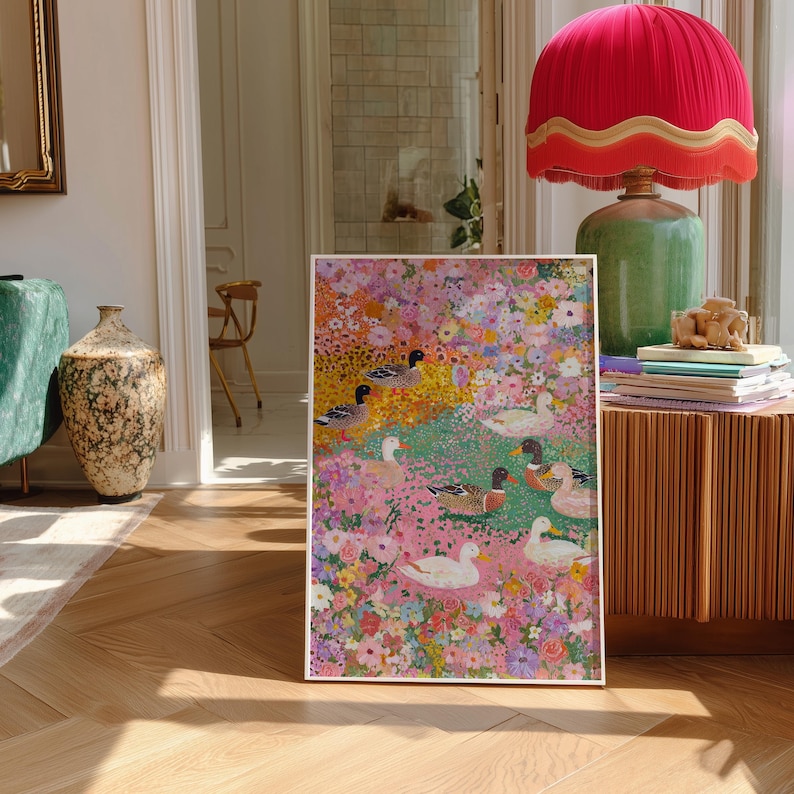 May include: A framed art print depicting a floral scene with ducks. The artwork features a vibrant mix of pink, yellow, and green hues, with several ducks scattered throughout the floral landscape. The print is displayed in a bright, well-lit room.