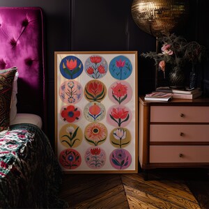 May include: A framed artwork featuring a collection of colorful floral illustrations in circular designs. The artwork is displayed in a room with a pink nightstand, a tufted headboard, and a gold disco ball.