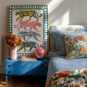 Four prowling leopards in vivid green, pink, sky-blue and indigo coats, each with whimsical floral patterns, stride across a cream backdrop. The bold dopamine palette enlivens living rooms, nurseries or eclectic gallery walls.