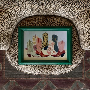 May include: A framed artwork featuring a collection of colorful cowboy boots. The boots showcase various patterns and designs, including floral, leopard print, and glitter. The green frame contrasts with the boots' colors.