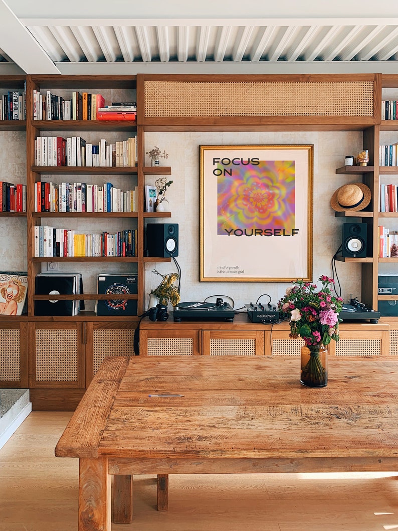May include: A wooden table with a light wood finish. The table has a natural wood grain pattern and is surrounded by a bookshelf, a record player, and a vase of flowers. A poster with the text "Focus on Yourself" is hanging on the wall behind the table.