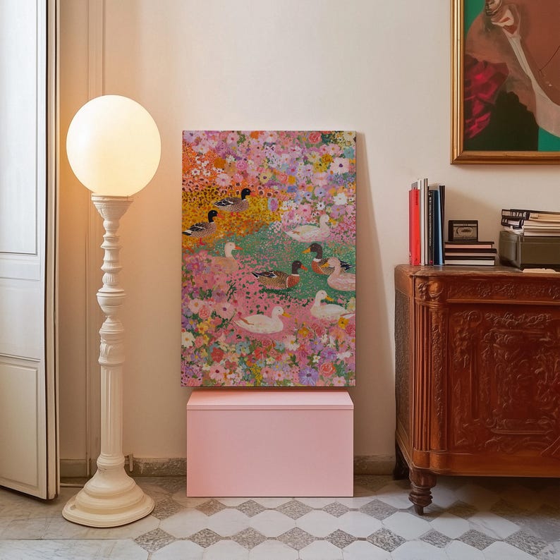 May include: A decorative white floor lamp with a globe-shaped light stands beside a painting of ducks in a floral setting. A pink box is beneath the painting, and a wooden cabinet is to the right. The painting is a vibrant display of colour.
