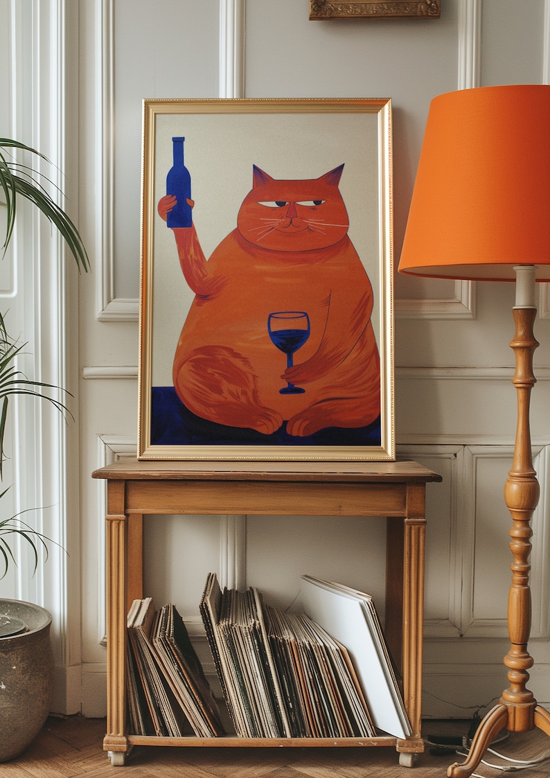 May include: A framed painting of an orange cat holding a glass of red wine and a blue bottle. The cat is sitting on a blue background. The painting is on a wooden shelf with a stack of vinyl records.