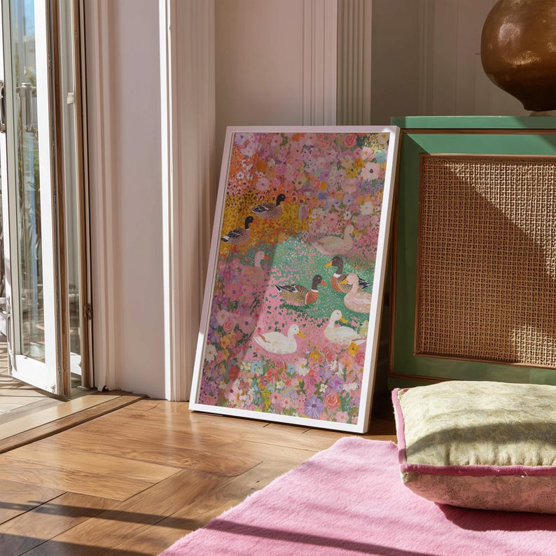May include: A framed art print with a floral and duck design. The artwork displays a vibrant mix of pink, yellow, and green hues, with several ducks and flowers. The print is encased in a white frame, adding a clean, modern touch.
