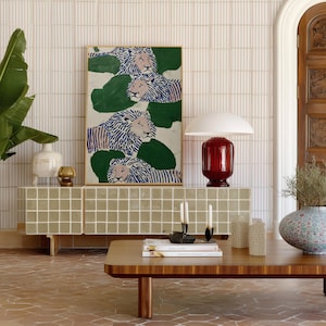 May include: A living room scene featuring a wooden coffee table, a tiled cabinet, and a framed artwork with lion illustrations. A red lamp and decorative vases add color. The floor is tiled in a terracotta color.