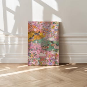 May include: A canvas print depicting a floral scene with ducks. The artwork features a vibrant mix of pink, yellow, and green hues, with detailed depictions of ducks swimming amidst the flowers. The print is displayed against a white wall and wooden floor.