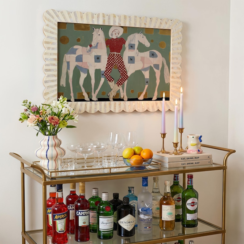 Modern western art print featuring a stylish cowgirl in a white hat and red polka dot outfit posed between two white patchwork horses. Soft sage green background with gold geometric accents and quilt-like horse patterns create a chic, editorial equestrian vibe. Perfect for contemporary western decor, ranch house interiors, cowgirl chic bedrooms, offices, and giftable horse lover wall art.