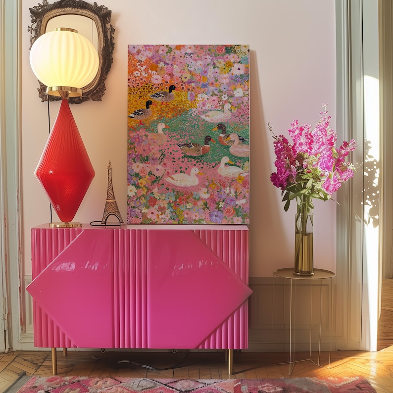May include: A bright pink cabinet with a diamond design and gold legs. A red diamond-shaped lamp and a painting of ducks in a floral setting are displayed on the cabinet. A small Eiffel Tower ornament and pink flowers are also present.
