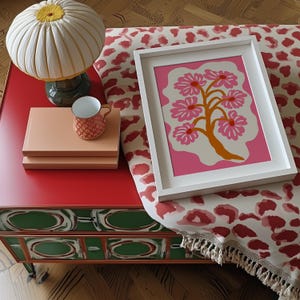 Flat-graphic illustration of a stylized orange tree trunk sprouting bright pink daisies on a cream blob shape against a vibrant pink background—cheerful, preppy and coquette-inspired.
