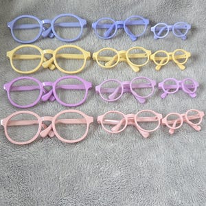 Może przedstawiać: Kolekcja kolorowych okularów w różnych rozmiarach. Oprawki są w odcieniach niebieskiego, żółtego, fioletowego i różowego. Okulary ułożone są w rzędach, prezentując różne style i rozmiary.