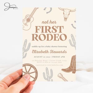 May include: A baby shower invitation with a western theme. The invitation features a guitar, a steer skull, a cowboy boot, and the text "not her FIRST RODEO". The invitation is held by a hand.