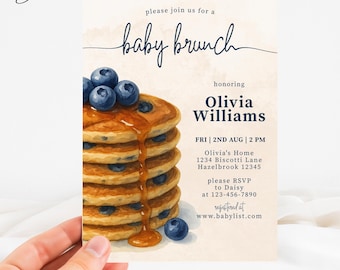 May include: Baby brunch invitation featuring a stack of pancakes with blueberries and syrup. The invitation text reads "baby brunch" and honors Olivia Williams. Details include date, time, and RSVP information. The invitation is held by a hand.