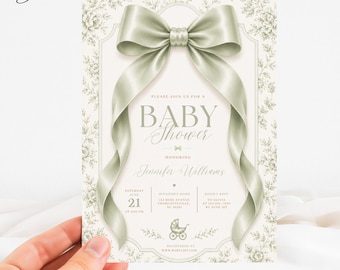 Può includere: Un biglietto d'invito rettangolare per baby shower con un grande fiocco in raso verde salvia sulla parte superiore. Il biglietto ha uno sfondo color crema con un delicato bordo floreale verde salvia, testo centrato e una piccola illustrazione.