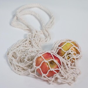 May include: Two red apples in a white string mesh bag. The bag is made of natural fibers and has a loose, open weave.
