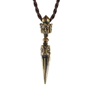 May include: A gold-colored metal pendant in the shape of a dagger with a detailed face at the top and a pointed tip. The pendant is hanging from a brown cord.
