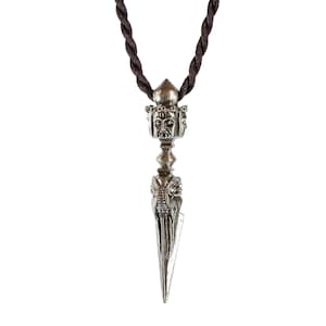 May include: A silver pendant necklace with a detailed, ornate design. The pendant features a pointed tip and a face with multiple eyes. The necklace is on a brown cord.