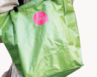 May include: A person carrying a green reusable shopping bag with a pink speech bubble logo that says "agidon".