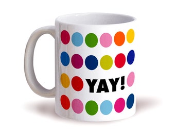 May include: White ceramic mug decorated with colorful polka dots in various colors, including blue, green, pink, and orange. The word "YAY!" is printed in black. The mug has a curved handle.