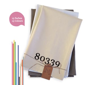 Könnte beinhalten: Drei natürliche Leinen-Geschirrtücher, die übereinander gestapelt sind. Das oberste Tuch ist weiß und hat die Nummer "80339" in Schwarz aufgedruckt. Ein braunes Etikett mit dem Text "Made with Love" ist um die Tücher gebunden.