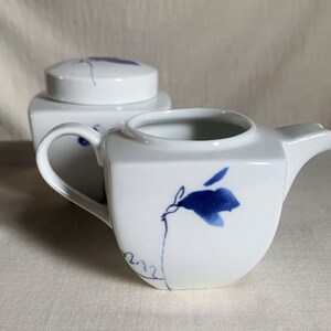 Peut inclure: Ensemble de crémier et sucrier en céramique blanche avec des motifs floraux bleus. Le pichet à crème a un corps carré et un bec courbé. Le sucrier a un corps carré et un couvercle.