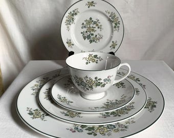 Puede incluir: Un juego de té blanco con estampado floral con una taza, un platillo y platos. El juego presenta un borde verde y un delicado diseño floral en amarillo, verde y azul. El juego incluye un plato llano, un plato de ensalada y un plato de pan.