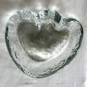 Può includere: Un piatto di vetro trasparente a forma di cuore con una superficie testurizzata. Il piatto è perfetto per contenere piccoli oggetti come gioielli o cianfrusaglie.