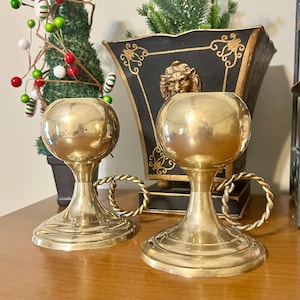May include: Two gold candle holders with a rope design. The candle holders have a round top and a wide base.