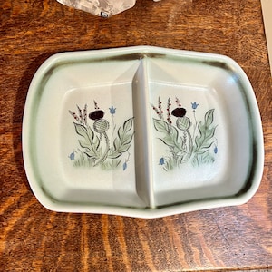 May include: A divided serving dish with a white background and a green and brown thistle design. The dish is oval shaped and has a raised rim.