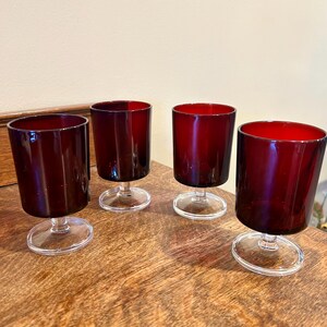 May include: Set of four ruby red glass stemmed drinking glasses. The glasses have a clear base and a deep red color.