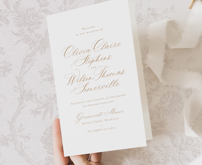 May include: Wedding invitation with a white background and gold text. The invitation reads "Welcome to the wedding of Olivia Claire Stephens and Wilson Thomas Somerville. Saturday, the seventh of September, two thousand twenty-four. Greencrait Manor, Battle Creek, Michigan. Our happily ever after."