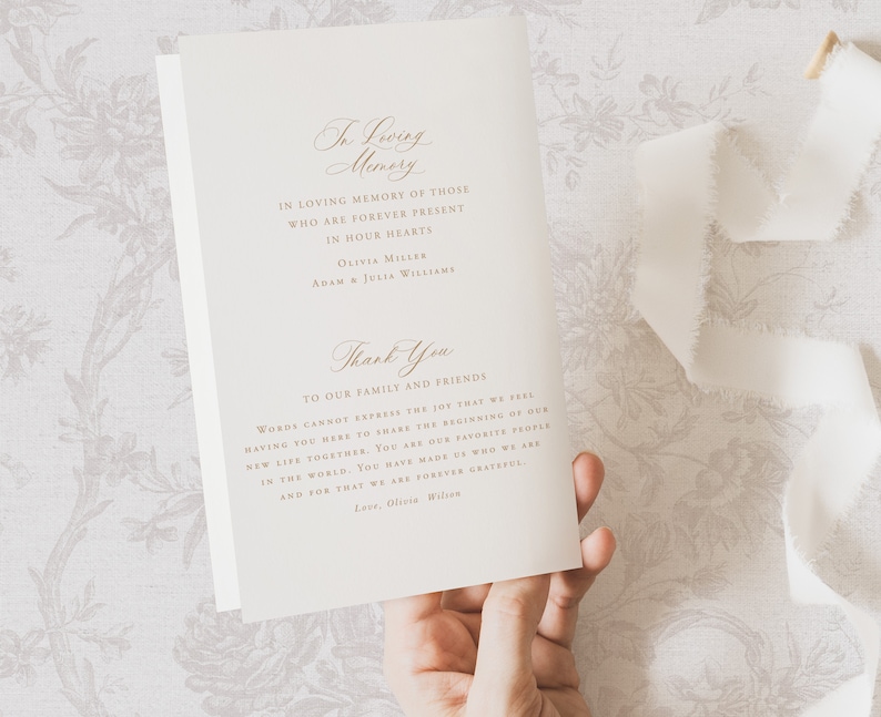May include: A white card with gold lettering that reads "In Loving Memory" and includes a thank you message to family and friends. The card is being held by a hand.