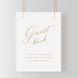 May include: White sign with a gold cursive font that says "Guest Book". Below the text, it says "Please sign and leave your wishes for the new Mr. and Mrs. Williams."